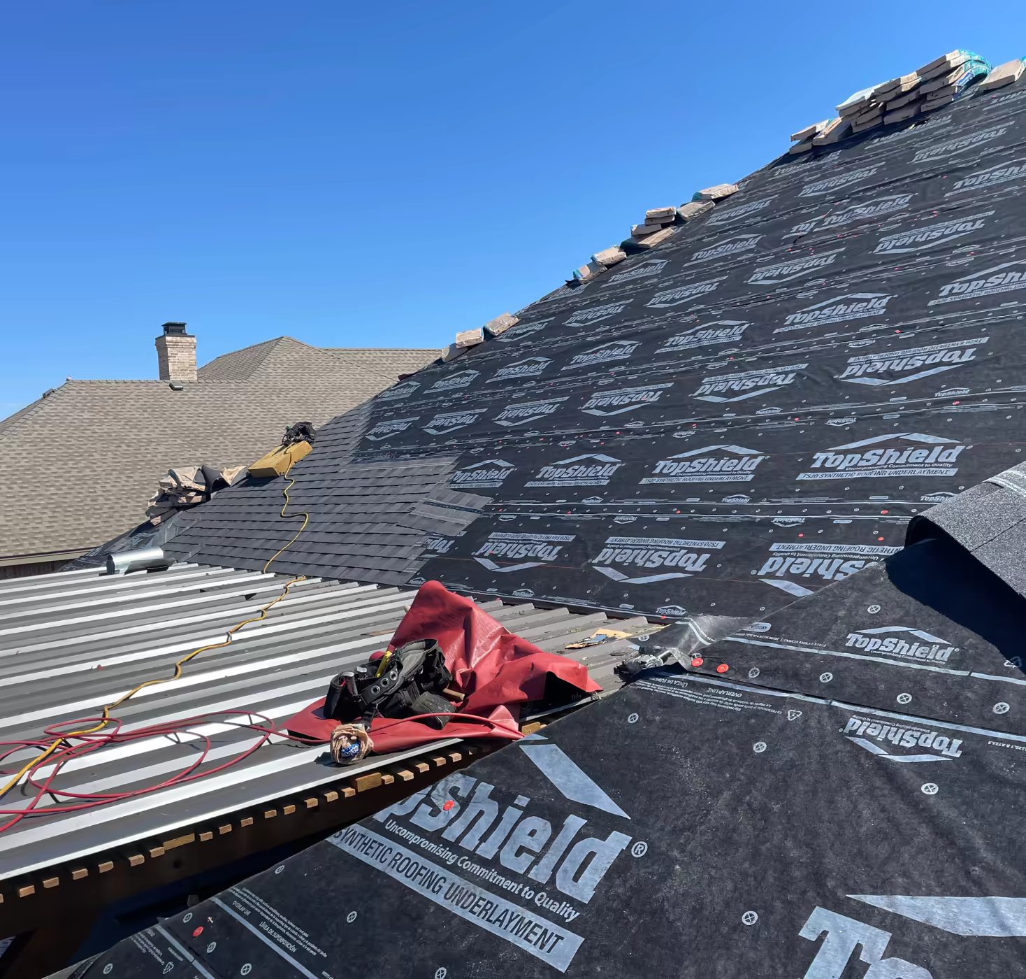 Roof-Tech crew replacing a residential roof under a clear blue sky